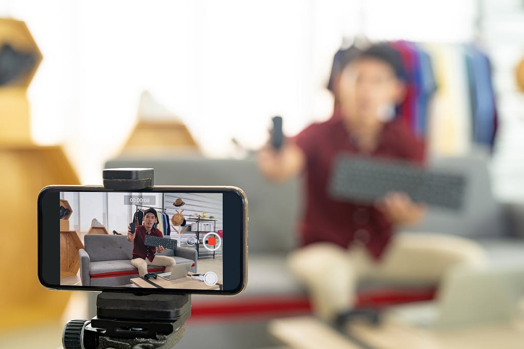 Young blogger using smart mobile phone to record live video to review IT product. The image is focused on mobile phone