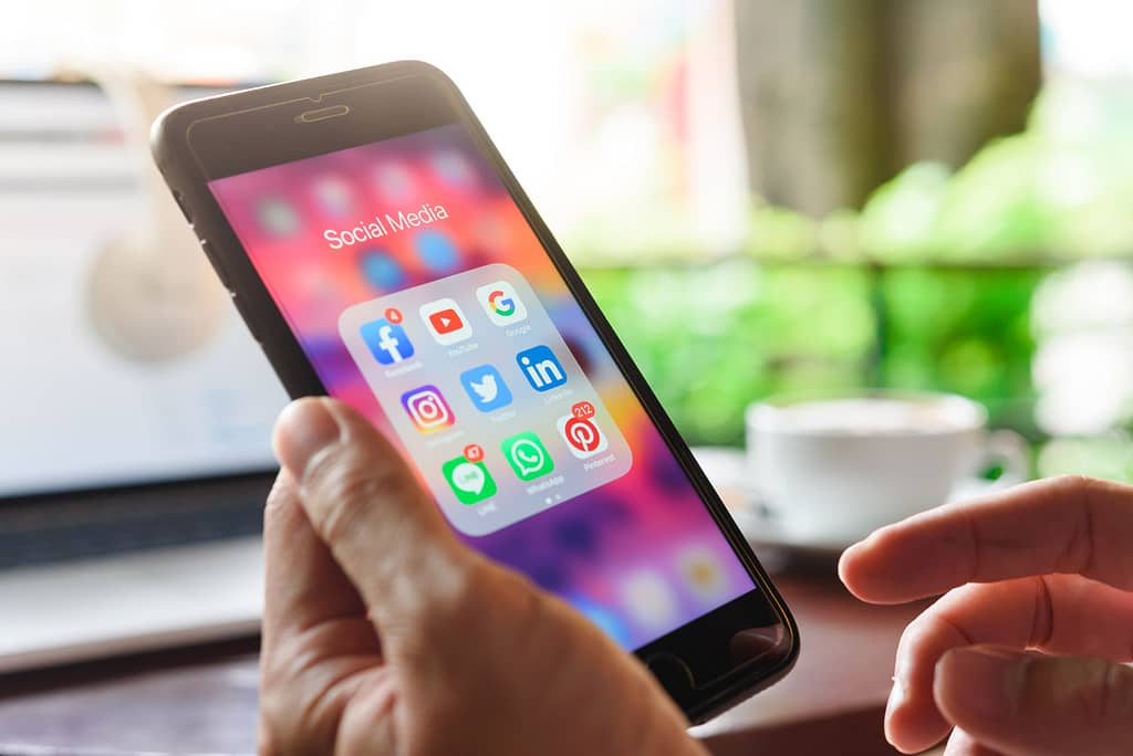 Hands hold an iPhone looking at several mobile apps, deciding which to select
