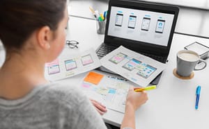 A woman overlooks a desk full of paper as she designs a custom mobile app